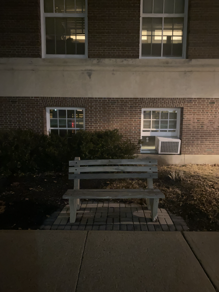 A photo of a bench in front of a building at night.